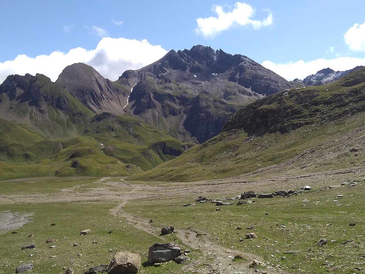 The footpath crossing a broad alpine basin of turf and scattered boulders below the Wurmaulspitze, a waymark painted on a rock beside it.