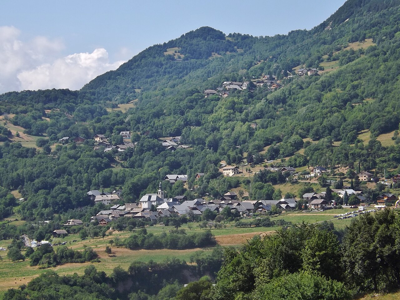 The village of Montvernier on its wooded shelf above the Maurienne, hay meadows below it and mixed woodland running up the slope behind.