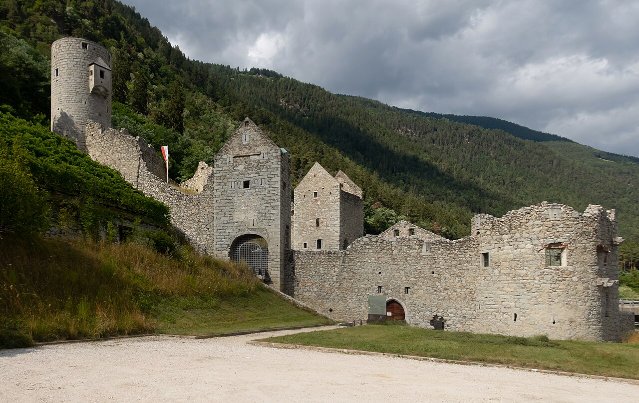 The Muehlbacher Klause, the medieval barrier wall and tower thrown across the valley, wooded slopes rising behind it under storm cloud.