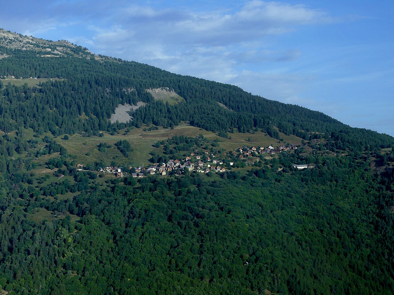 The hamlet of Albanne on its wooded shelf above the Maurienne in September, pasture and spruce running up the slope behind it.