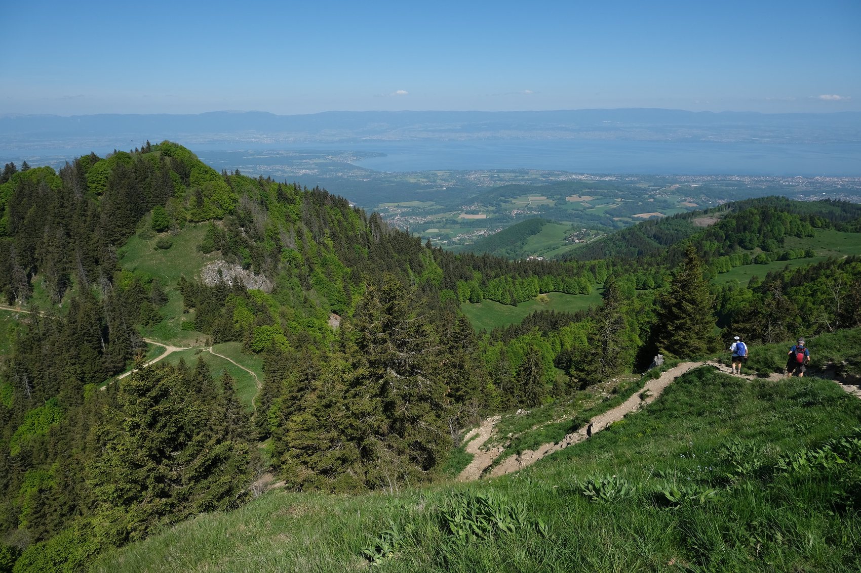 Two walkers on the grass path along the Mont Forchat ridge above the Chablais foothills with Lake Geneva beyond