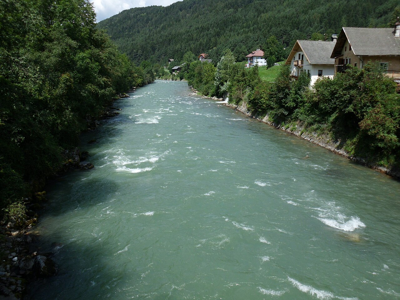 The green water of the Rienz running between wooded banks below houses at Kiens.