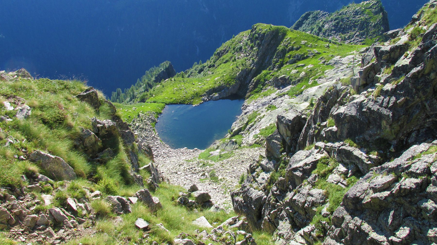 The Lago Negro tarn in its granite cirque below Cima d'Asta with grass and scree on the slopes above