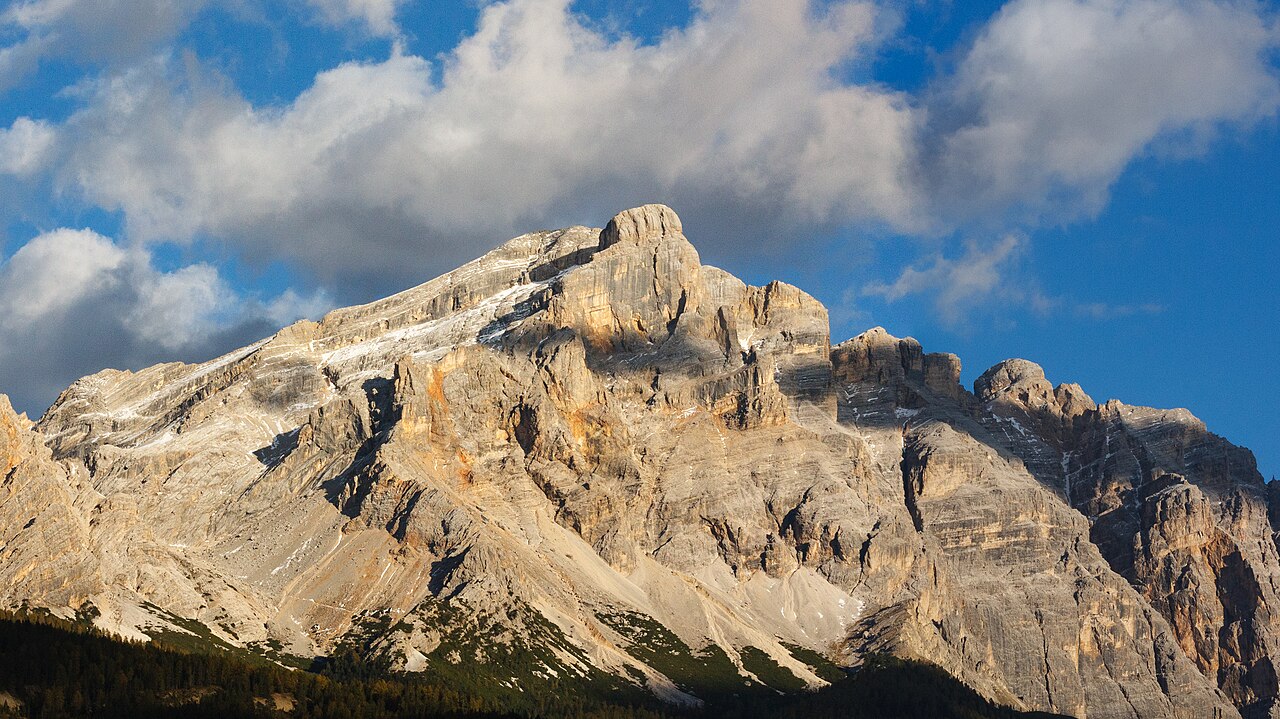 The banded limestone wall of Piz Lavarela above Alta Badia in evening light, forest along the foot of the cliffs.